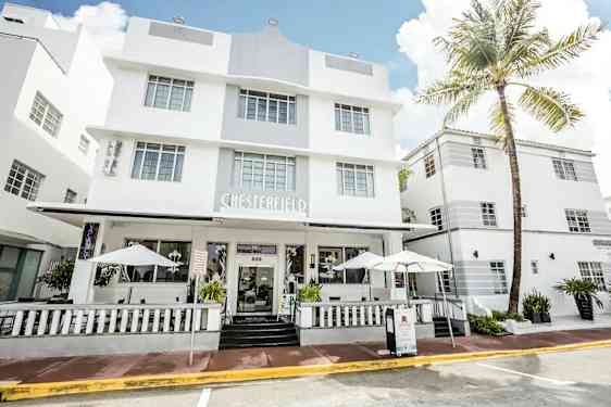 Et hvidt hotel i moderne arkitekturstil med store vinduer og en veranda med parasoller. (AI-genereret tekst)