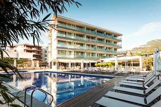 Billede af et hotel med swimmingpool og liggestole udendørs. (AI-genereret tekst)