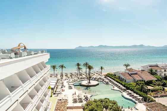 En udsigt over hotelpool, strand og hav med palmer og bygninger. (AI-genereret tekst)