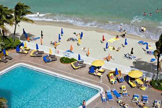 En strand med liggestole, parasoller og badende mennesker samt en pool med omkringliggende liggestole. (AI-genereret tekst)