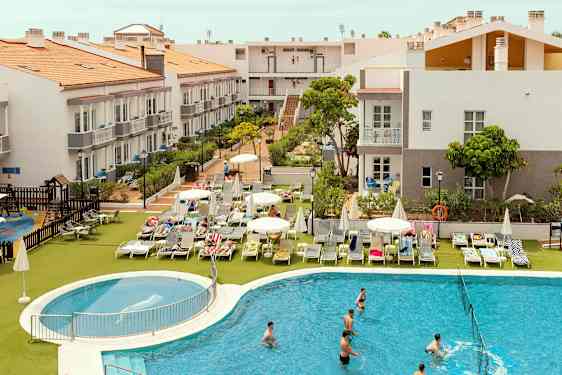 Hotelområde med bygninger, liggestole og en pool. (AI-genereret tekst)