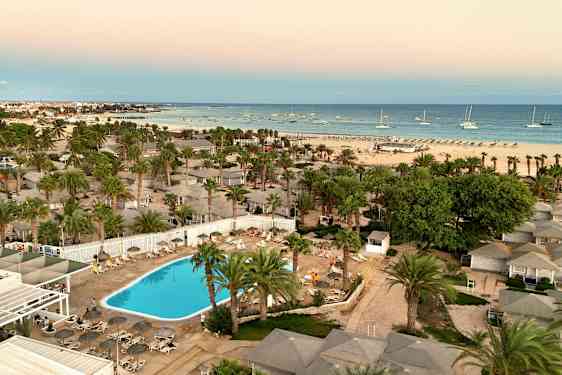 Luftfoto af hotelområde med pool, palmer og en strand i baggrunden. (AI-genereret tekst)