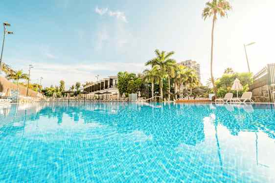 Billede af en udendørs pool omgivet af palmer og liggestole. (AI-genereret tekst)