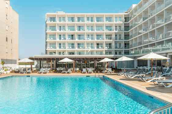 En bygning med flere altaner, foran en pool med liggestole og parasoller. (AI-genereret tekst)