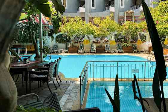 En swimmingpool med liggestole og parasoller i en have. (AI-genereret tekst)