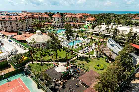 Oversigtsbillede af en ferieanlæg med hoteller, swimmingpools, legeplads og haver tæt på havet. (AI-genereret tekst)