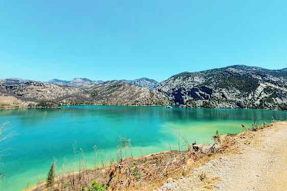 Et billede viser en klar turkis sø omgivet af bjerge under en skyfri himmel. (AI-genereret tekst)