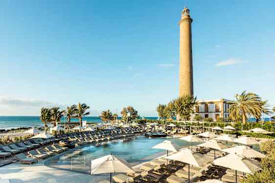 En solrig resort med pool, liggestole og parasoller samt et fyrtårn i baggrunden. (AI-genereret tekst)