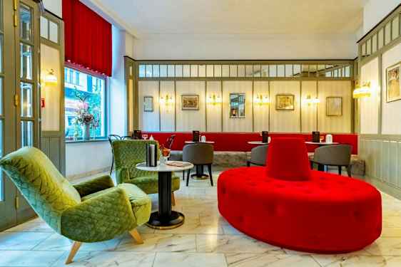 En hotellobby med siddeområde, inklusive grønne lænestole, røde og grå sidemøbler og marmorgulv.  (AI-genereret tekst)