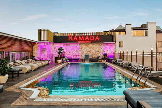 Billede af en udendørs pool med liggestole omkring og et skilt med teksten Ramada by Wyndham. (AI-genereret tekst)