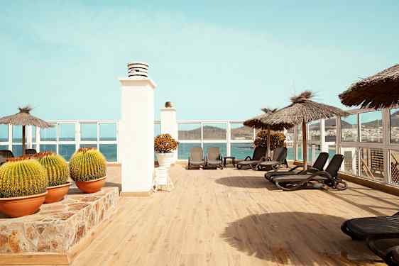 Terrasse med liggestole, parasoller og udsigt over havet. (AI-genereret tekst)