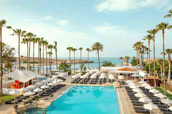 Billede af en pool med liggestole, parasoller og palmer ved en strand. (AI-genereret tekst)