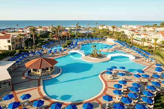 Udendørspool omgivet af liggestole og parasoller samt hotelbygninger i baggrunden mod havet. (AI-genereret tekst)