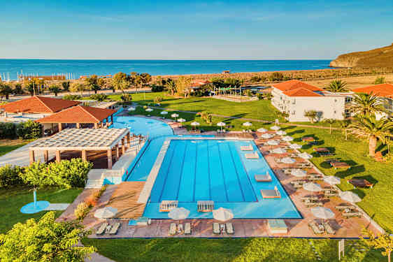 Udendørs pool med liggestole og parasoller, frodig græsplæne og havet i baggrunden. (AI-genereret tekst)