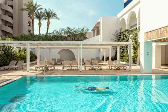 En udendørs pool med liggestole ved siden af og en person, der svømmer i vandet. (AI-genereret tekst)