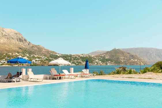 Udendørs pool med liggestole og parasoller samt udsigt til hav og bjerge. (AI-genereret tekst)