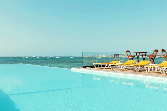 Pool med udsigt over havet og liggestole ved siden. (AI-genereret tekst)