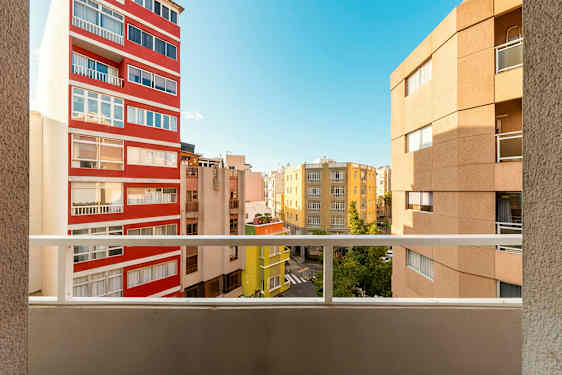 Udsigt fra en altan med flere bygninger og en blå himmel i baggrunden. (AI-genereret tekst)