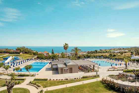 Hotelområde med to swimmingpools, liggestole og havudsigt. (AI-genereret tekst)