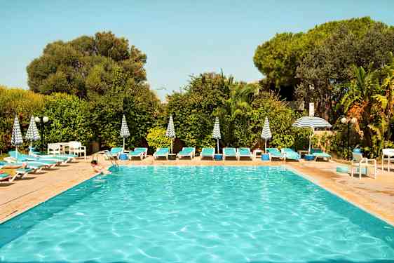 Udendørs pool omgivet af liggestole, parasoller og grønne planter. (AI-genereret tekst)