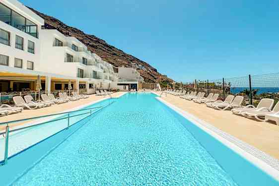 En pool ved et hotel med hvide bygninger og solvogne. (AI-genereret tekst)