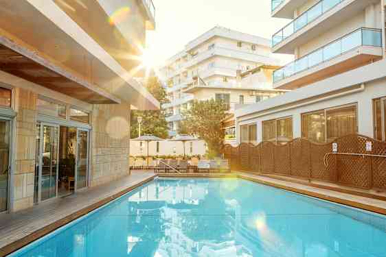 Udendørs pool med omkringliggende liggestole og bygninger. (AI-genereret tekst)