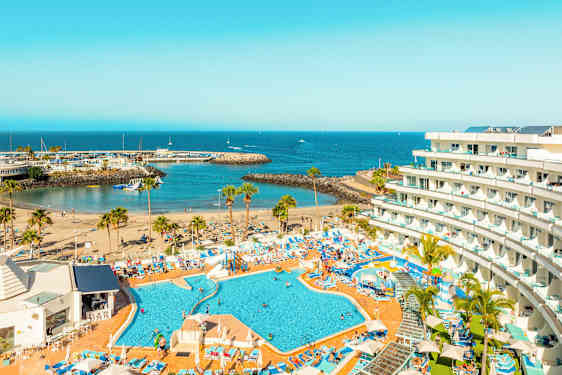 Billede af et hotel med poolområde, strand og havneindløb ved havet. (AI-genereret tekst)
