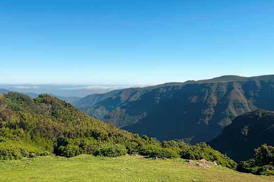 Billedet viser et landskab med frodige bakker og bjerge under en klar blå himmel. (AI-genereret tekst)