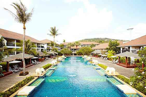 En stor pool på et feriested omgivet af palmer, liggestole og bungalowlignende bygninger. (AI-genereret tekst)