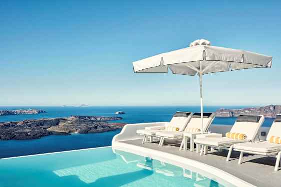 Solterrasse ved en infinitypool med udsigt over havet og klipper i baggrunden. (AI-genereret tekst)