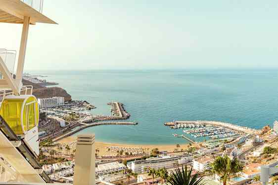 Udsigt over en havn og strand ved havet, set fra en højde med en gondol i forgrunden. (AI-genereret tekst)