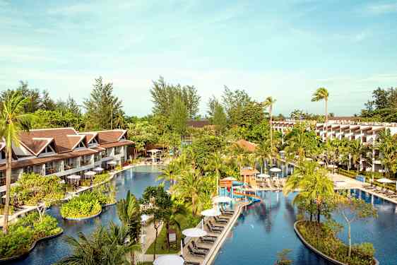 Hotelområde med en stor pool omgivet af palmer og bygninger. (AI-genereret tekst)