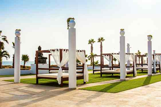 Udendørsområde med baldakinsenge og statue ved havet. (AI-genereret tekst)