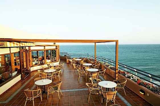 En terrasse med borde og stole og udsigt over havet. (AI-genereret tekst)