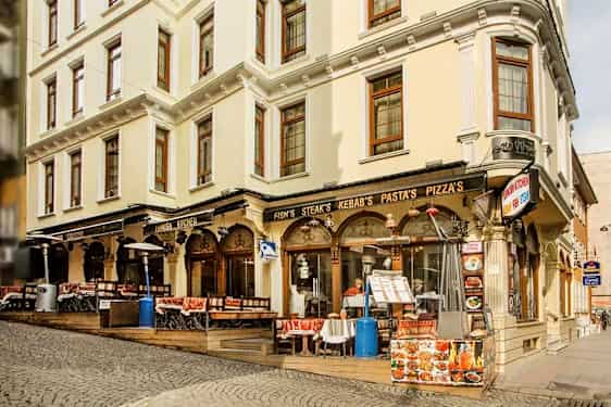 En gade med en bygning med restaurant og udendørs servering, skilte med mad som kebab og pizza. (AI-genereret tekst)