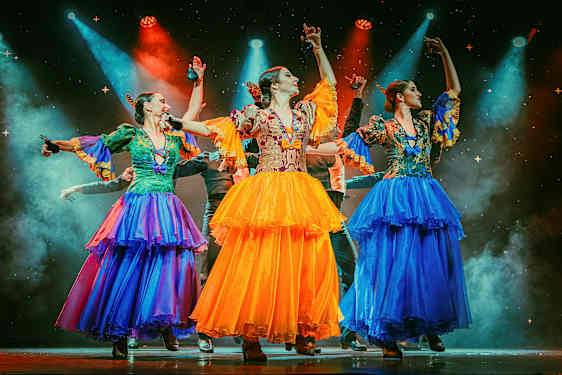 Tre personer iført farverige traditionelle dragter danser på en oplyst scene. (AI-genereret tekst)