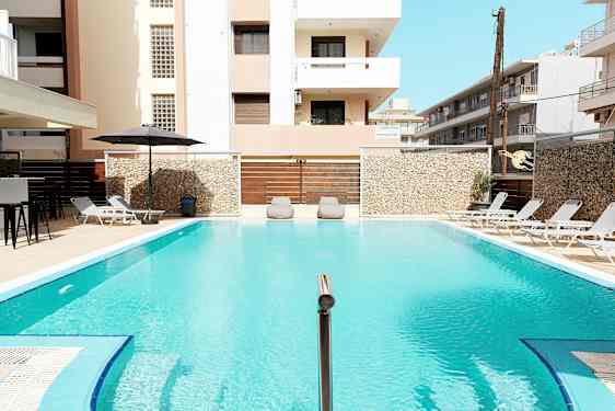 En udendørs pool omgivet af liggestole og bygninger. (AI-genereret tekst)