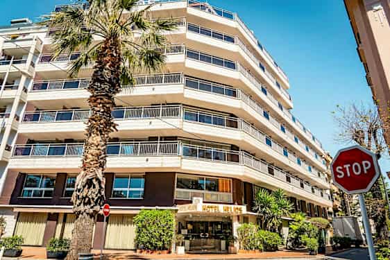 Et hotel med flere etager og et palmetræ foran. Skiltet "STOP" er synligt til højre. (AI-genereret tekst)