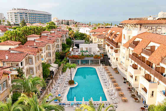 Hotelområde med en pool omgivet af liggestole og bygninger med røde tage. (AI-genereret tekst)