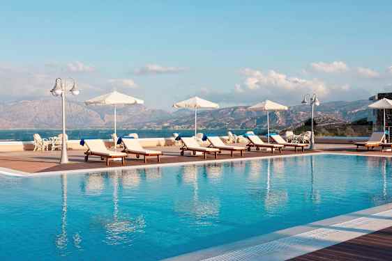 Liggestole og parasoller ved en udendørs pool med udsigt til bjerge og hav. (AI-genereret tekst)