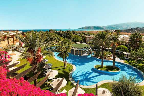 Billede af hotelområde med en stor pool og palmer samt udsigt ud mod havet. (AI-genereret tekst)