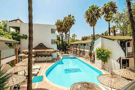 Udendørs pool omgivet af hvide bygninger og palmer. (AI-genereret tekst)