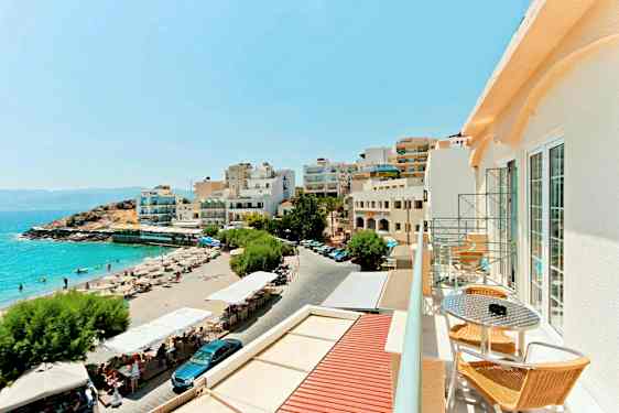 Udsigt over en sandstrand med liggestole og parasoller ved siden af bygninger med udsigt over havet. (AI-genereret tekst)