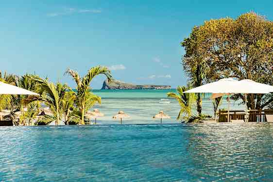 En infinitypool med udsigt over en strand med parasoller og en lille ø i havet. (AI-genereret tekst)