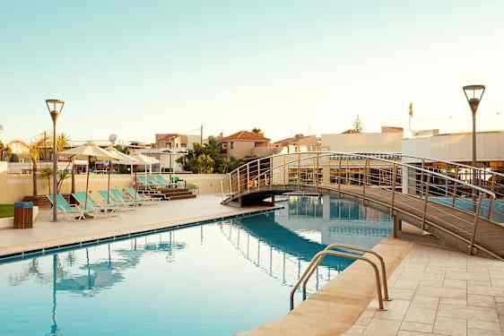 En udendørs swimmingpool med solsenge og en gangbro over vandet. (AI-genereret tekst)