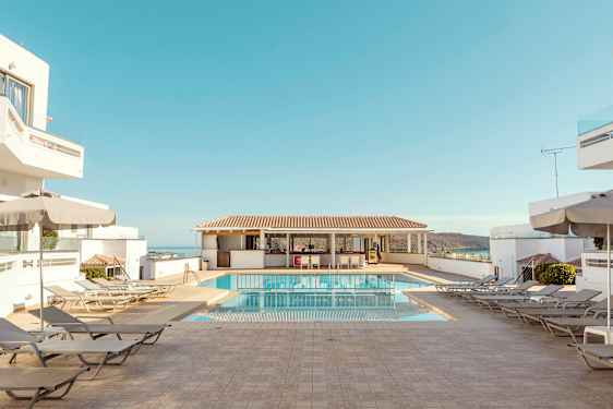 Hotelpoolområde med liggestole, parasoller og blå himmel. (AI-genereret tekst)