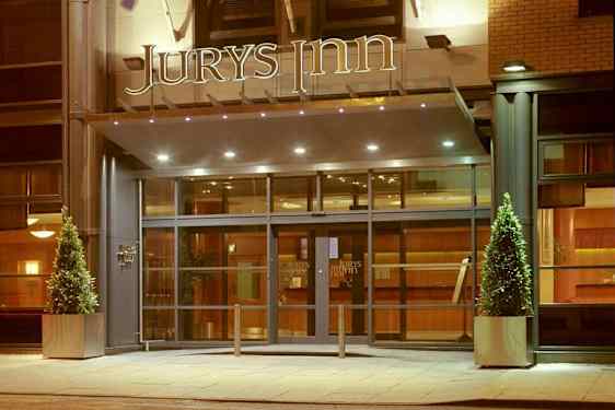 Hotelindgang med glasdøre og skiltet 'Jurys Inn' ovenfor. (AI-genereret tekst)