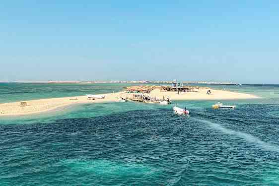 En lille sandø med både ved broen, omgivet af klart blåt vand. (AI-genereret tekst)