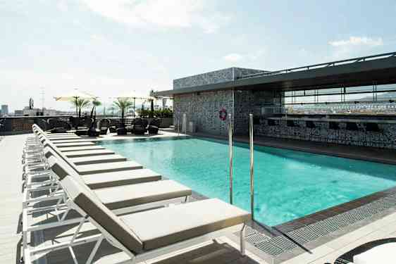 Billede af en solrig tagterrasse med en pool omgivet af liggestole og parasoller. (AI-genereret tekst)