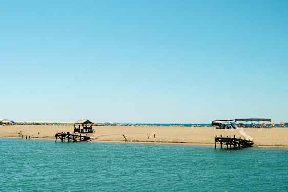 En strand ved havet med liggestole og parasoller samt en træbro. (AI-genereret tekst)